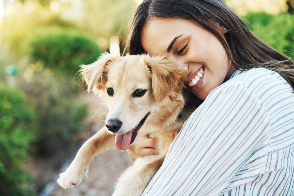 Frau umarmt lachend ihren Hund im Freien.