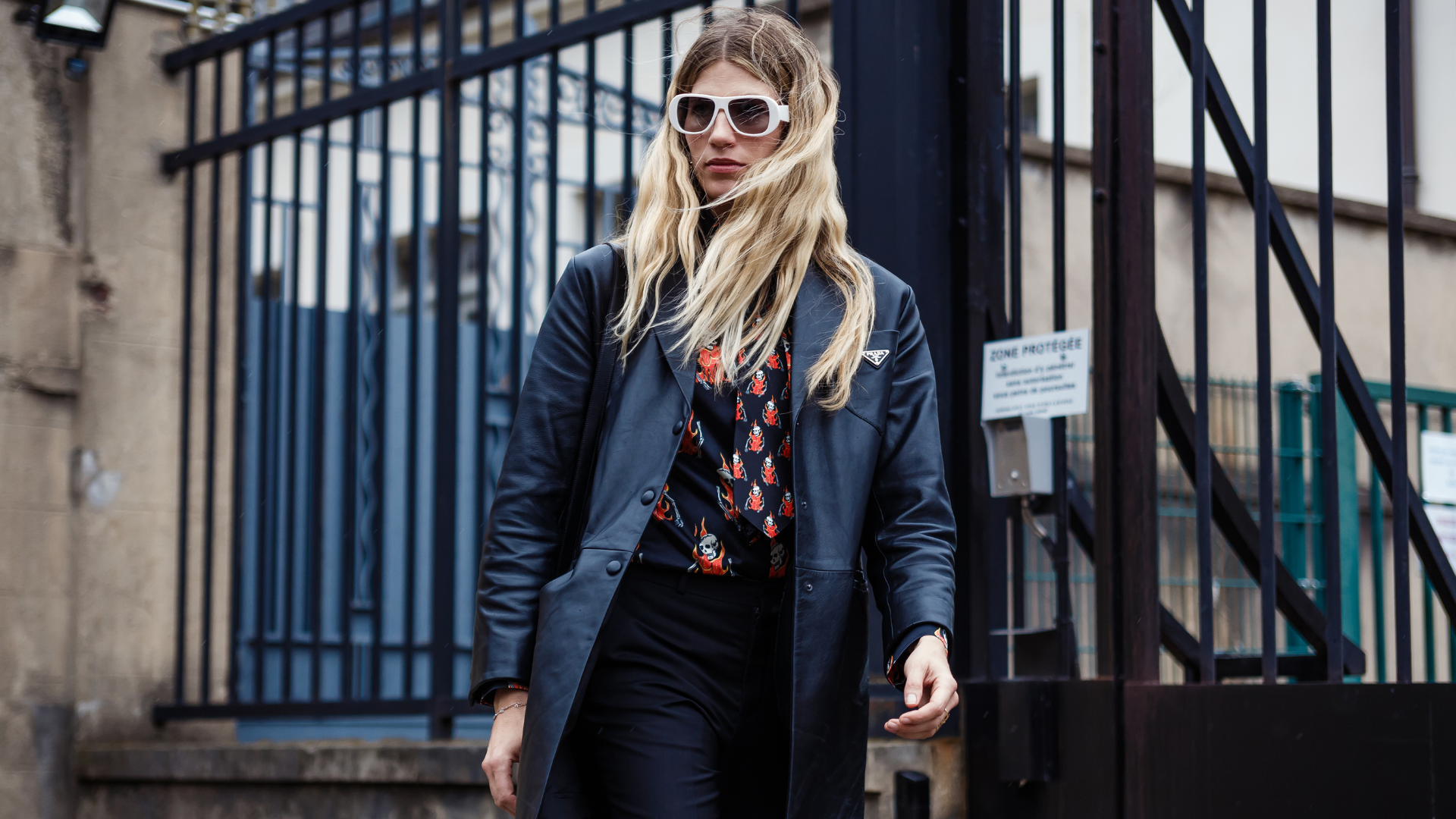 Streetstyle Look von Veronika Heilbrunner: langer Lack-Mantel, Strick mit Muster und weiße große Sonnenbrille