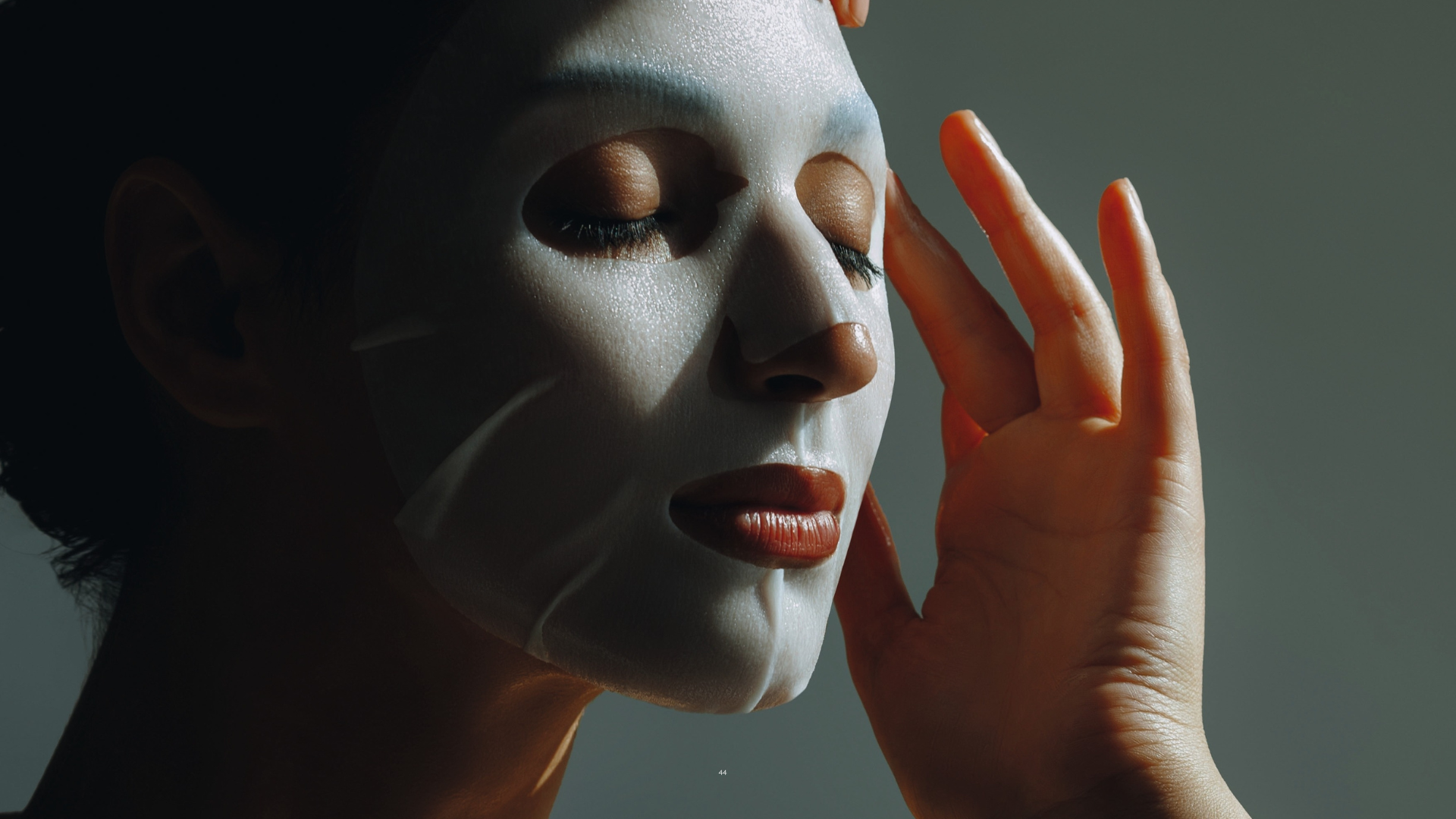 Hautfplege im Einklang mit dem Zyklus, Young beautiful woman applies white sheet mask to her face. Skin care, moisturizing and cleansing. Sunlight. Beauty and fashion portrait.