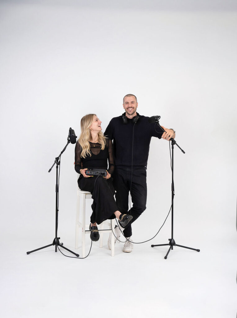 Podcast: Cornelia und Manuel Morgen vor weißer Wand mit stehenden Mikros.