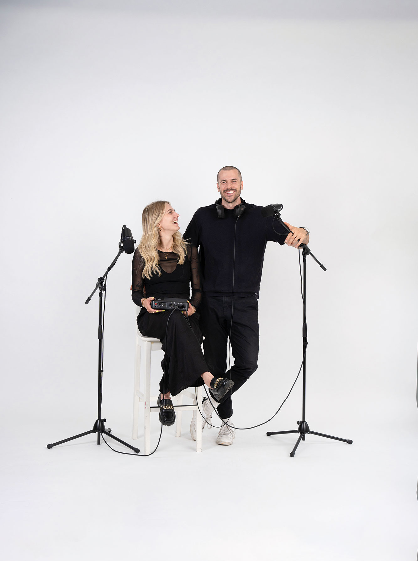 Podcast: Cornelia und Manuel Morgen vor weißer Wand mit stehenden Mikros.