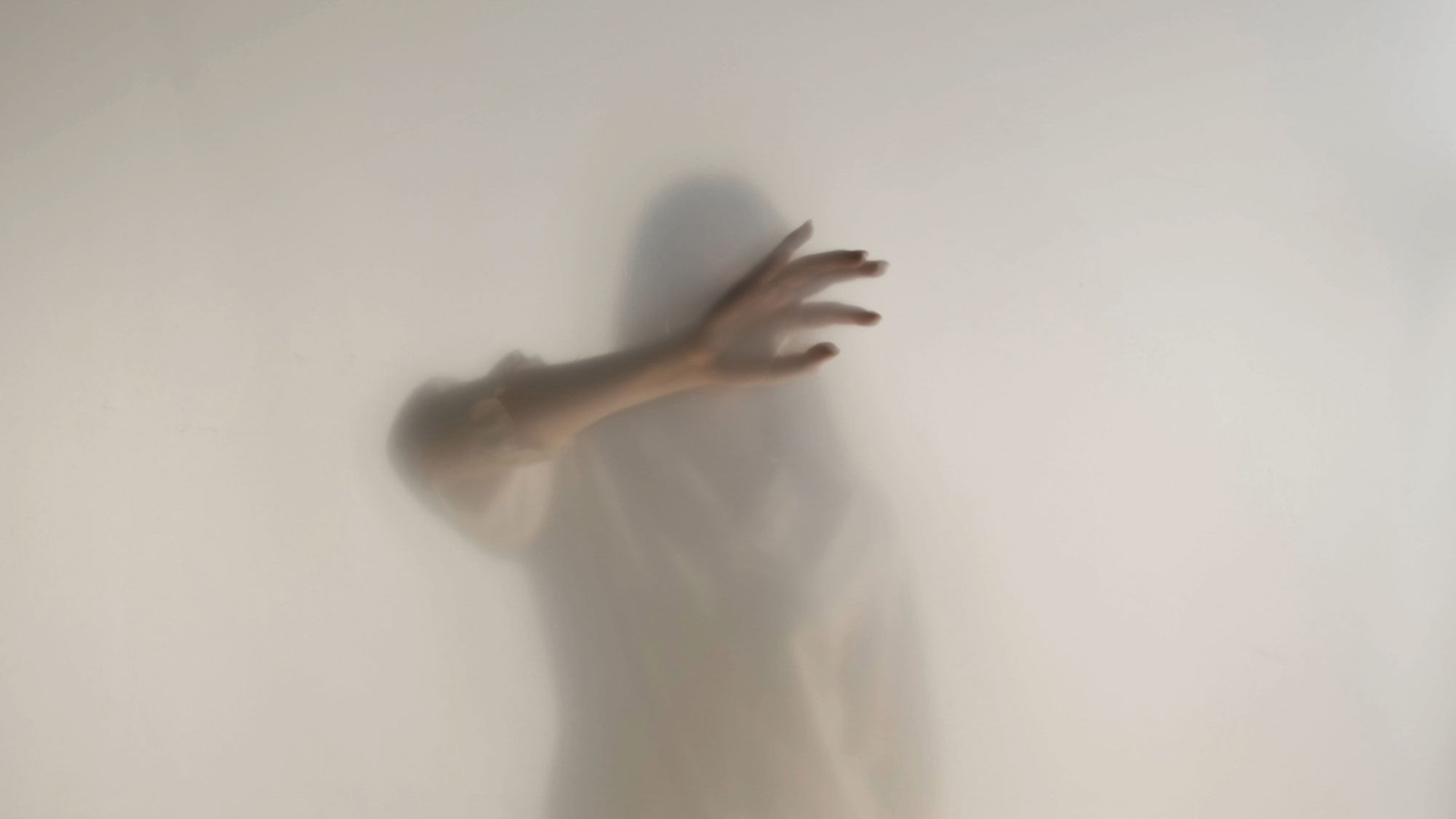 Frau hält Hand vors Gesicht hinter weiß verschleierter Wand.