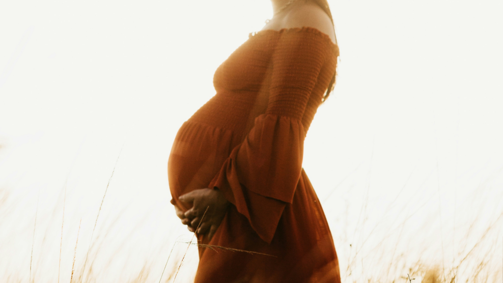 Eine Schwangere Frau in rotem Kleid hält ihren Bauch