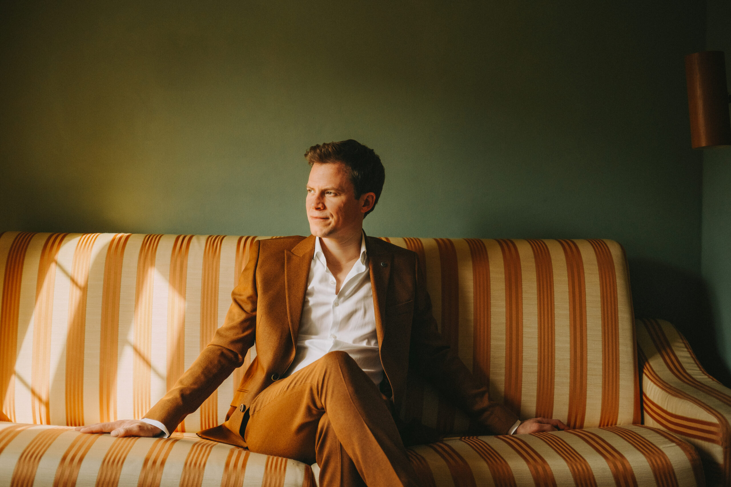 Tobias Pötzelsberger sitzt auf einem gestreiften Sofa, Porträtbild