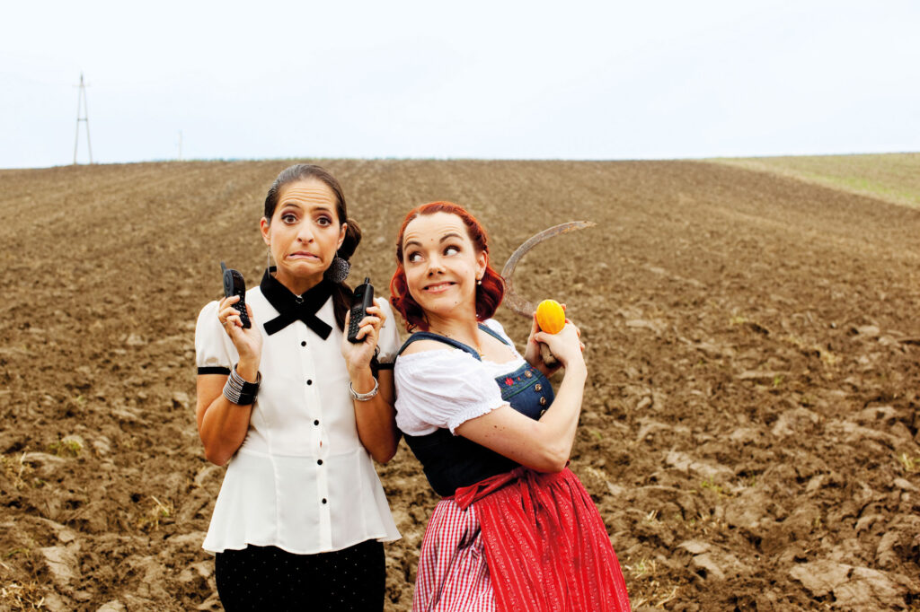 Caroline Athanasiadis und Gudrun Nikodem-Eichenhardt stehen mit Requisiten auf einem Feld.