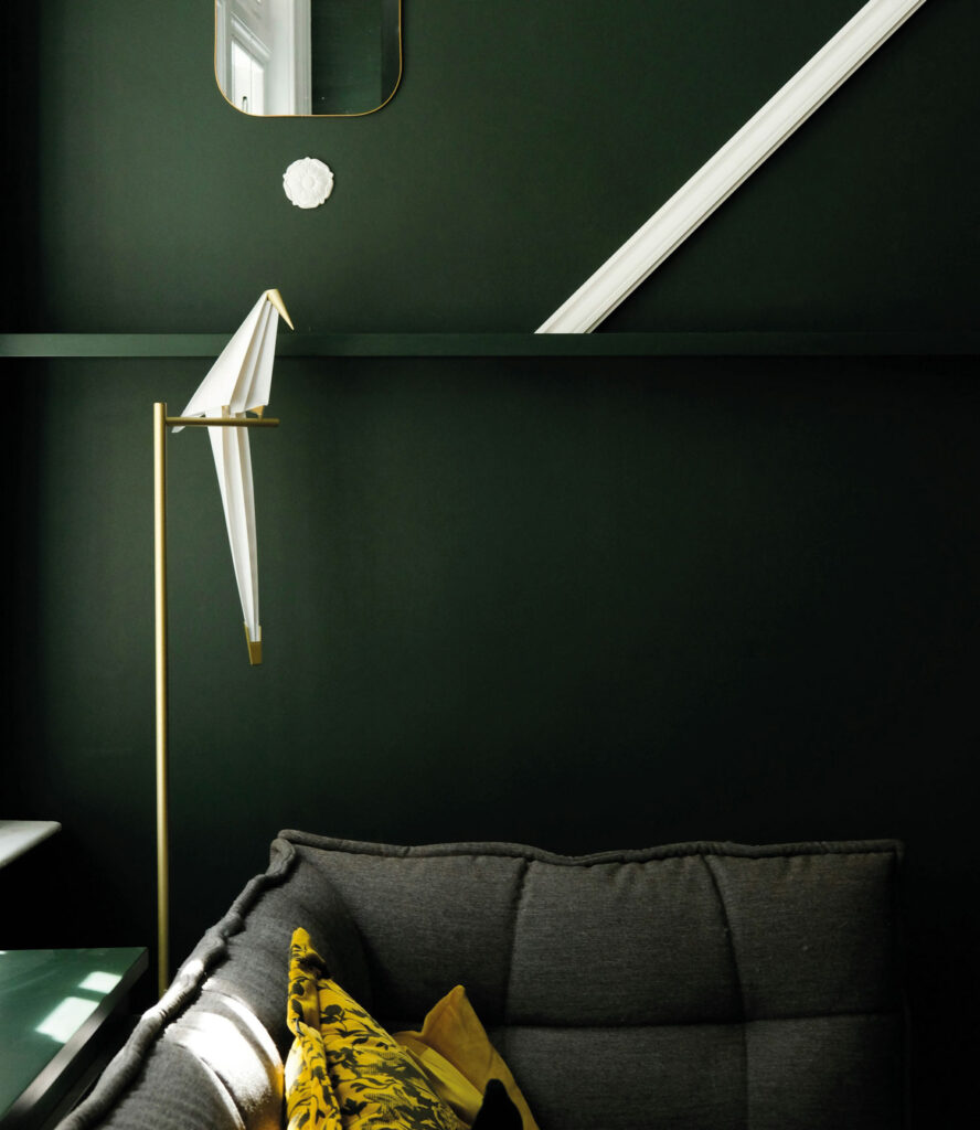 Dunkelgrüne Wand mit matschgrünem Sofa, gelbem Polster und einigen hellen Deko-Elementen.