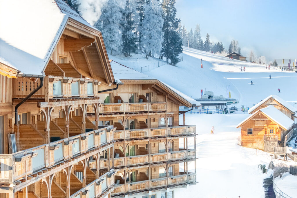Hölzernes, mehrstöckiges Gebäude direkt neben einer Skipiste vom Natur- & Wellnesshotel Höflehner ****Superior in der Region Schladming-Dachstein.