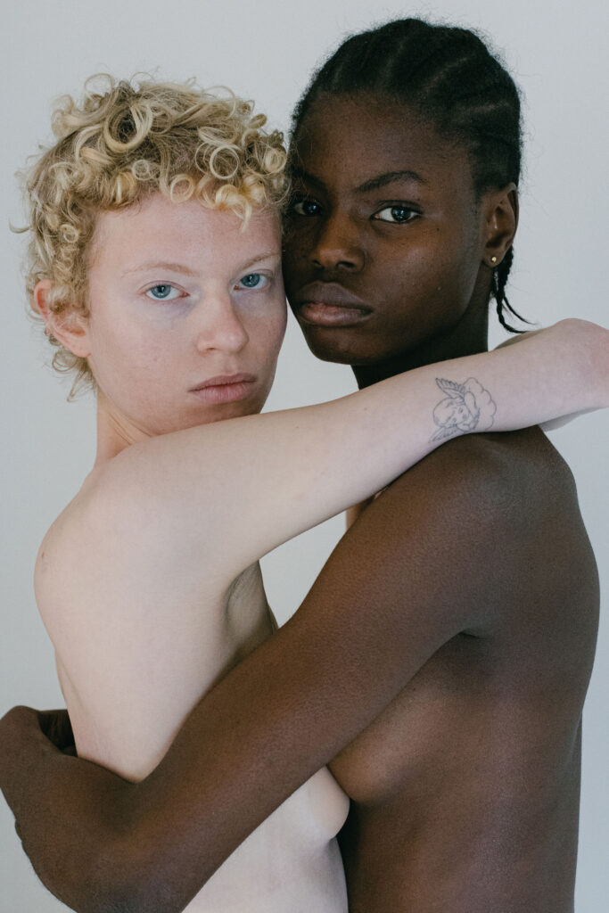 Akt-Foto von einer weißen und einer dunkelhäutigen Frau, die sich umarmen.