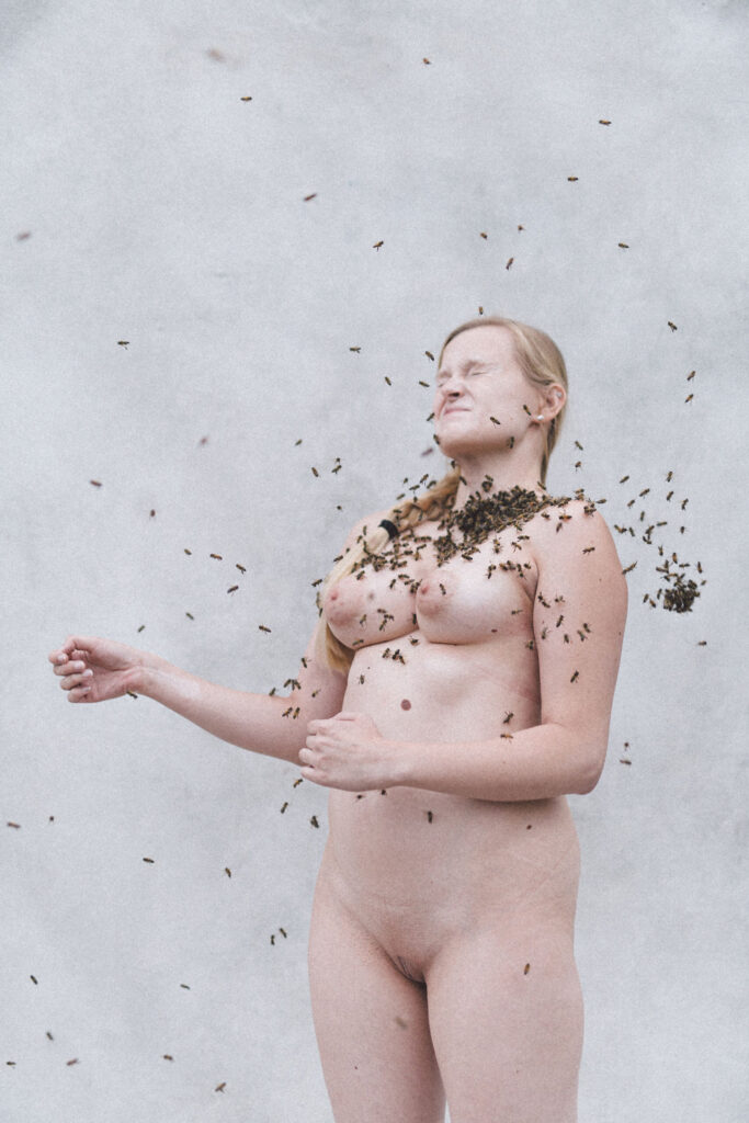 Akt-Foto von einer hellen Frau, die von Bienen umschwärmt wird.