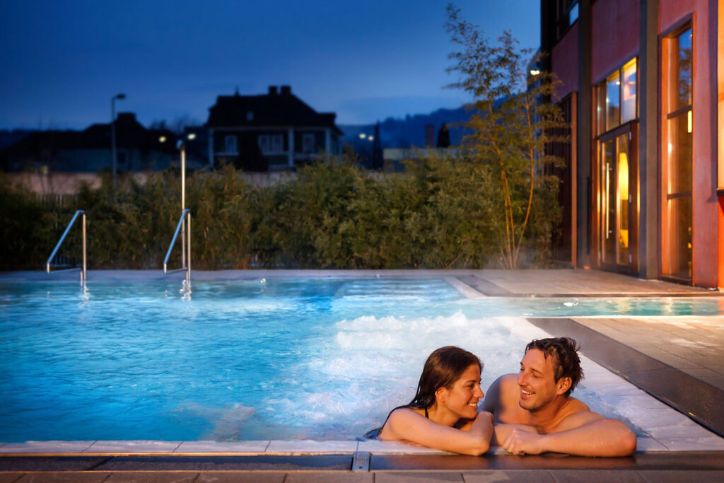 Asia Spa Leoben: Eine Frau und ein Mann entspannen sich in einem sprudelnden Thermalbecken im Freien am Abend.