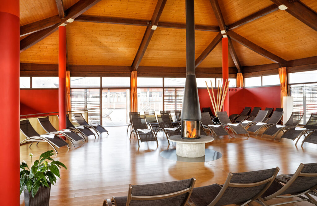 Ruheraum mit vielen leeren Liegen und einem brennenden Kamin in der Mitte.