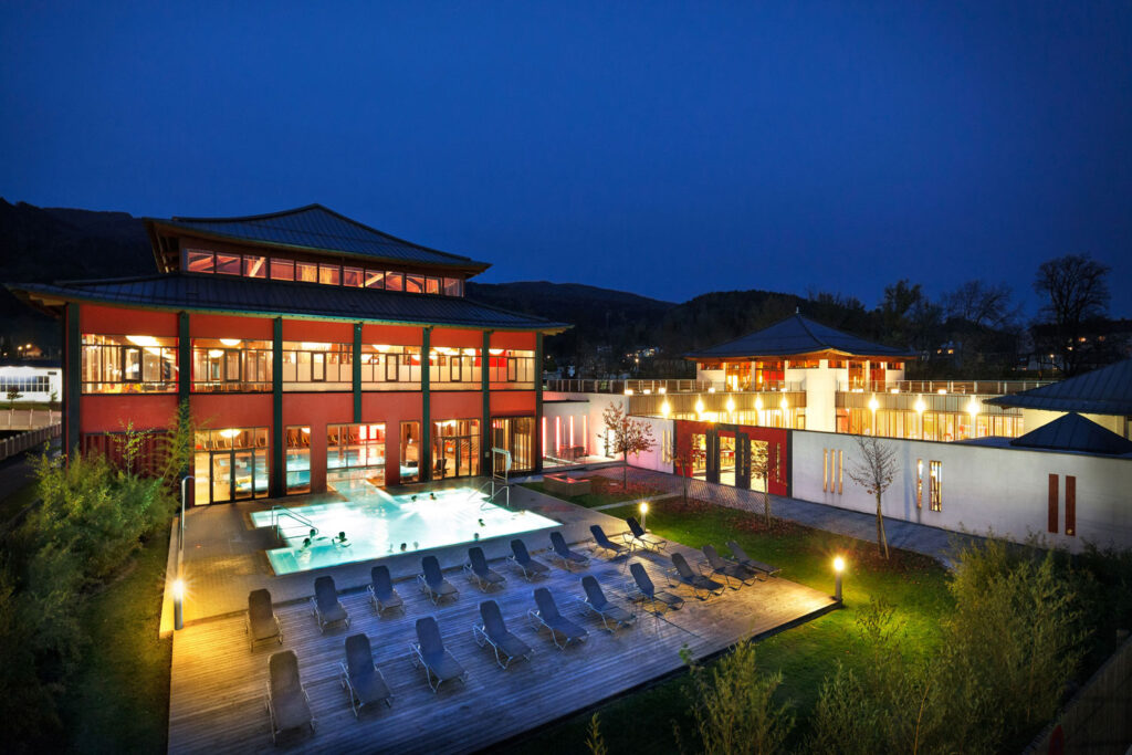 Abendliche Außenansicht vom Asia Spa Leoben mit Thermalbecken und Liegen im Freien