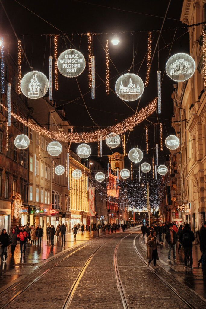 Die Herrengasse in Graz ist abends weihnachtlich beleuchtet und voll mit Menschen.