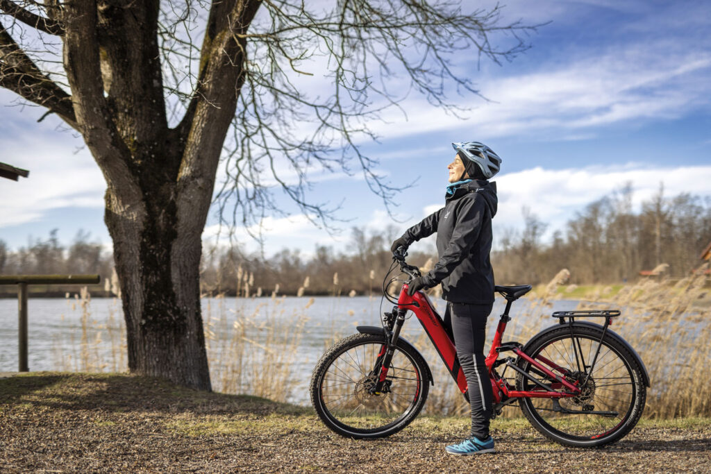 Eine sportliche Dame macht beim Winterradeln im Freien vor einem See eine Pause und atmet tief ein.