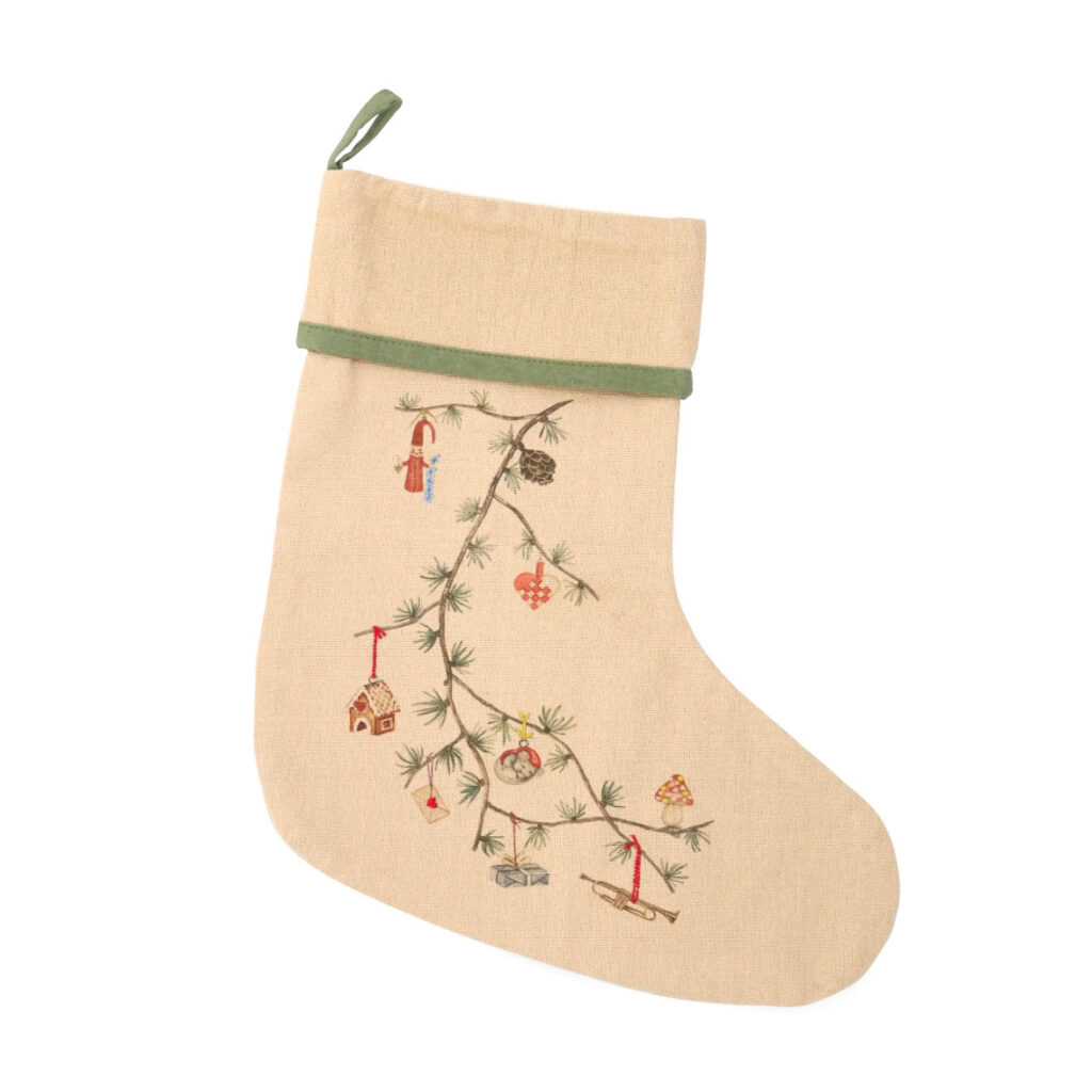 Ein beiger Weihnachtsstrumpf mit einem Tannenzweig von dem weihnachtliche Ornamente hängen.