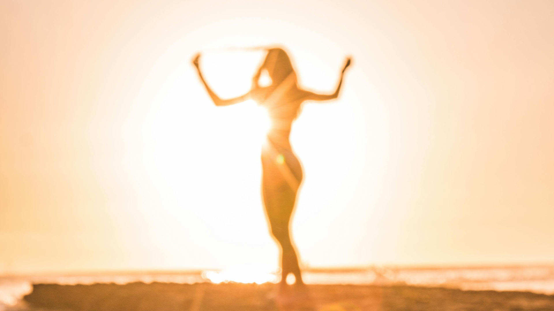 Frau am Strand wird von der Sonne im Hintergrund erleuchtet