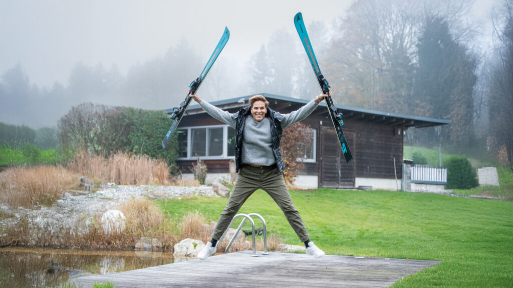 Michaela Dorfmeister: Frau springt mit Skiern in den Händen im Garten vor einem Haus.