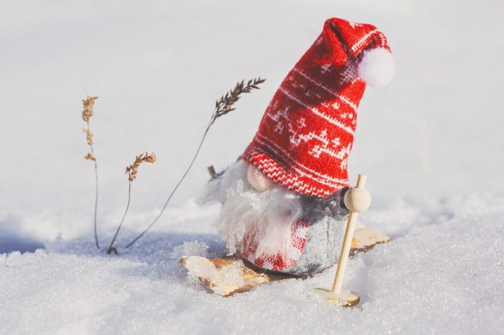 Ein Wichtel mit roter Mütze steht auf Skiern im Schnee
