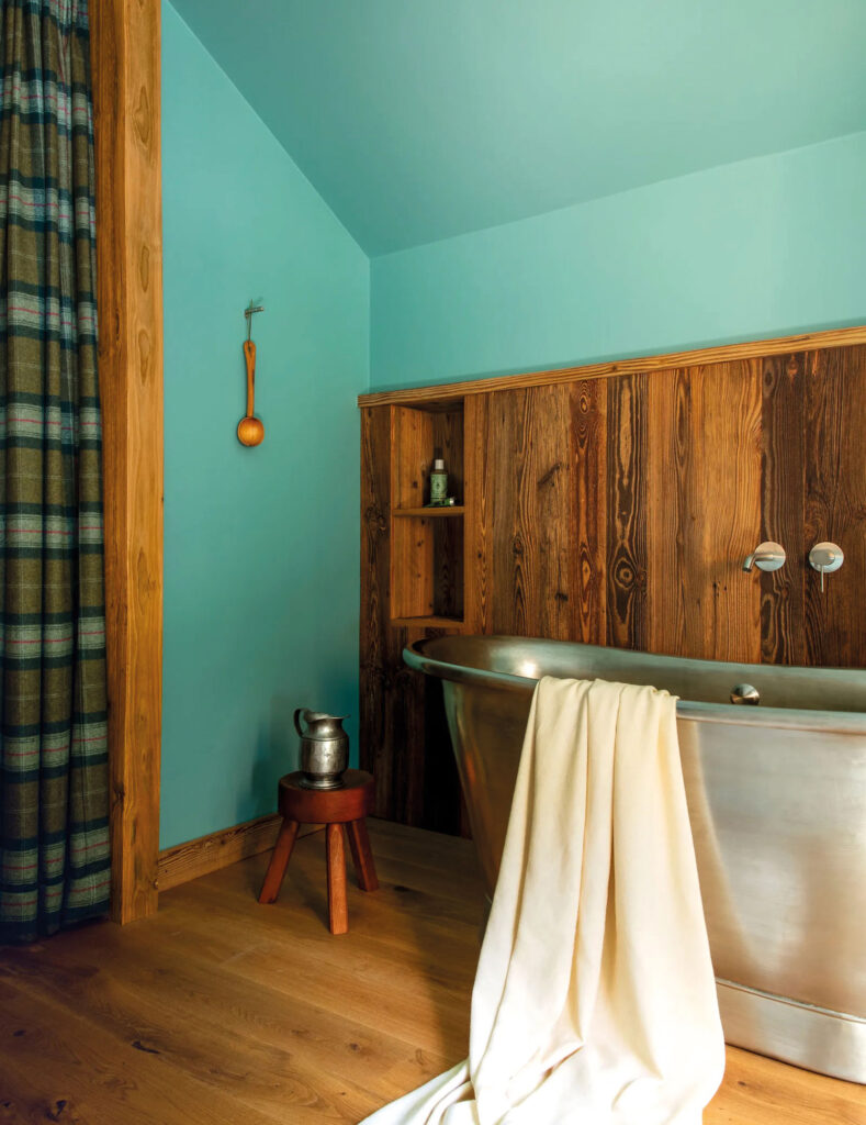 Türkise Wand mit Holz-Möbeln und freistehender Metall-Badewanne.