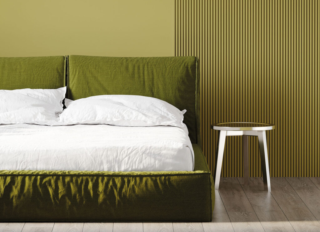 Dunkelgrünes Stoffbett mit weißer Bettwäsche vor hellgrüner Wand.