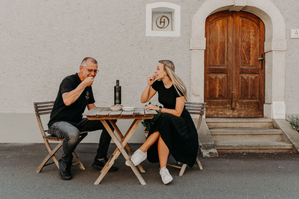 Eine Frau und ein Mann verkosten Öl vor einem alten Gebäude.