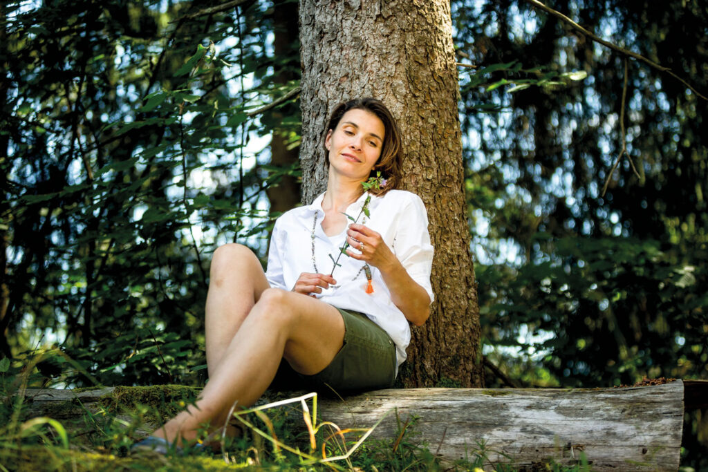 Evi Schmidt sitzt im Wald mit einer Blume in der Hand