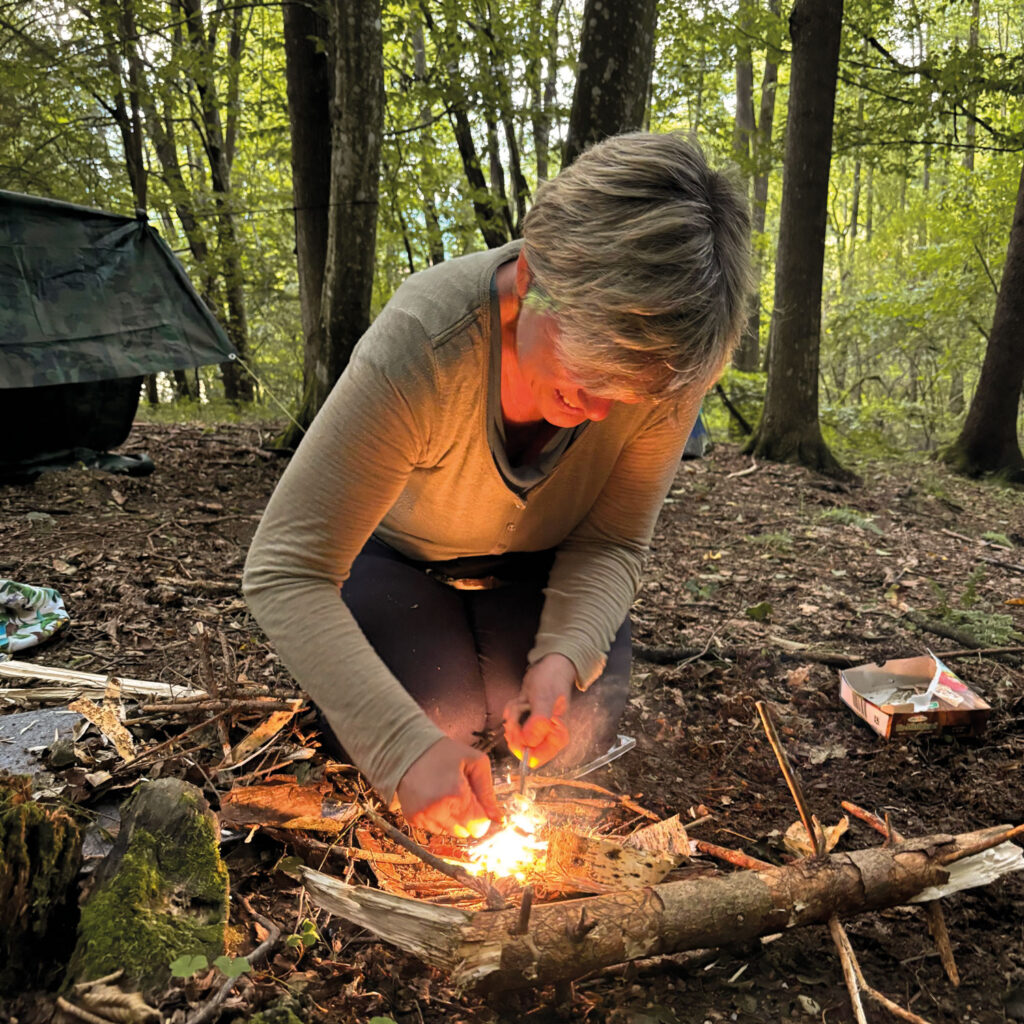 Eine Frau zündet im Wald ein Feuer an.