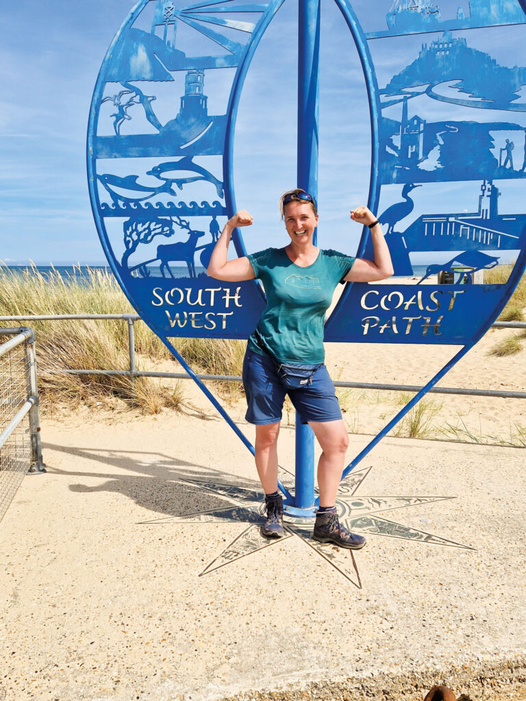 Doris Hollnbuchner vor einem großen blauen Schild an der Küste von Südengland.
