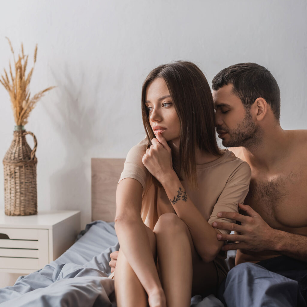 Keine Lust: Pärchen sitzt im Bett, der Mann versucht sie zu umarmen und die Frau schaut nachdenklich zur Seite.