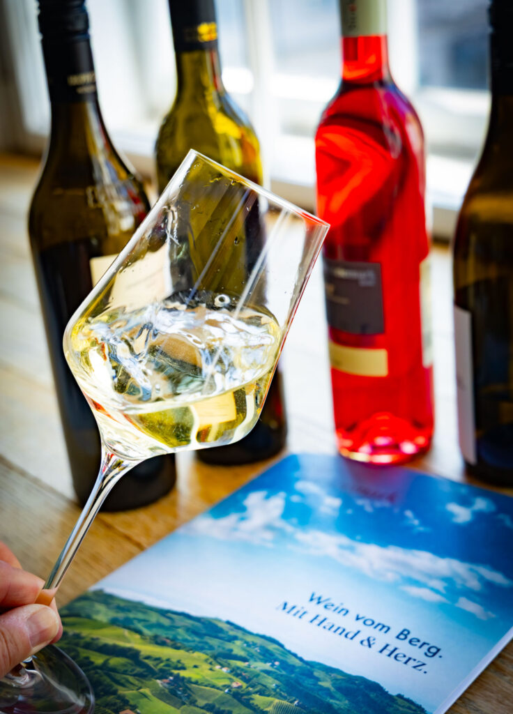 Ein gefülltes Weinglass mit mehreren Flaschen Wein im Hintergrund bei der Präsentation von Wein Steiermark.