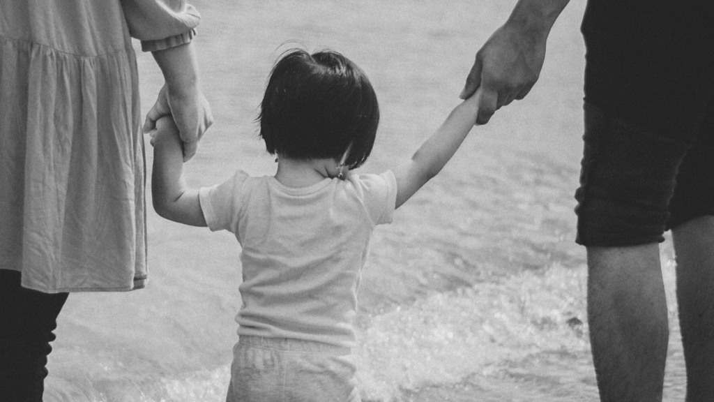 Ein Kind wird links und rechts an der Hand gehalten und geht einen Strand entlang