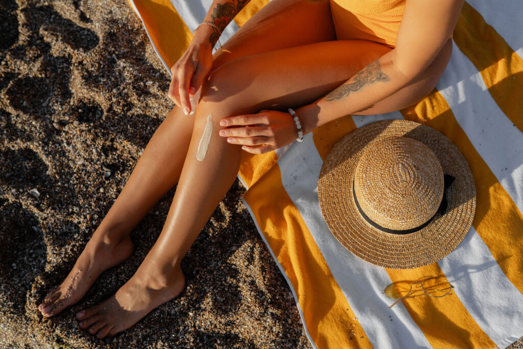 Frau trägt Sonnenschutz an den Beinen am Strand auf.