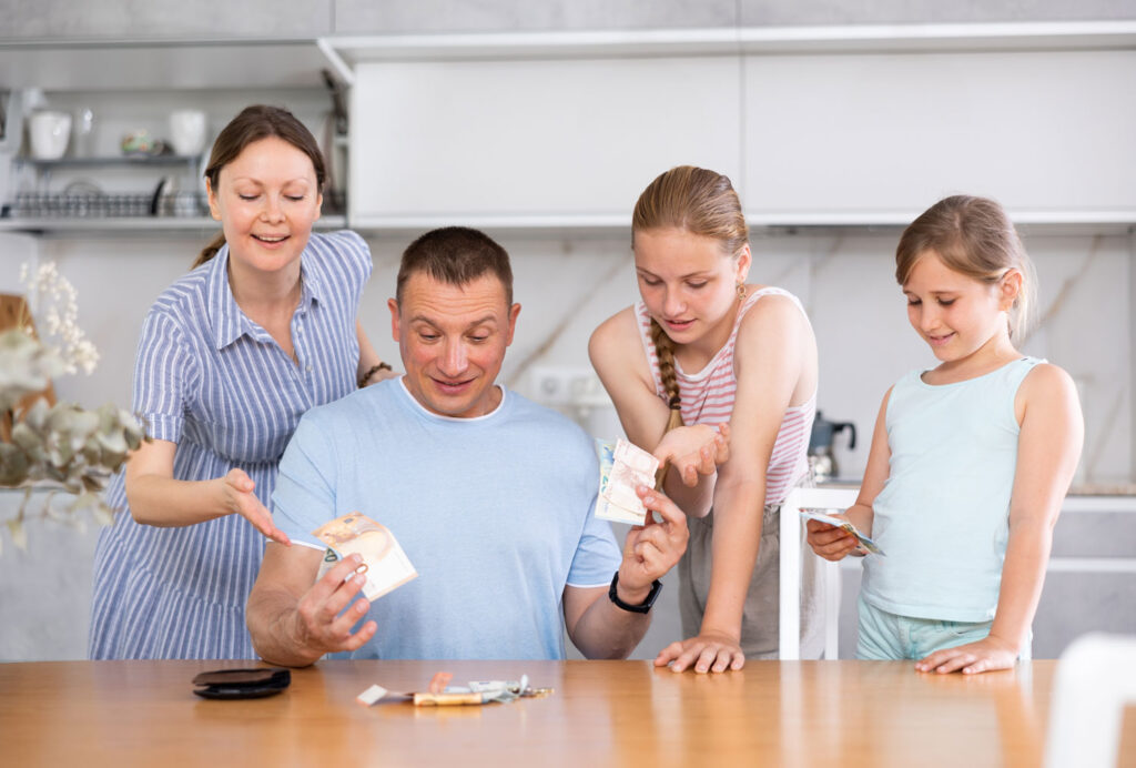 Vater verteilt in der Küche Taschengeld an seine Familie.