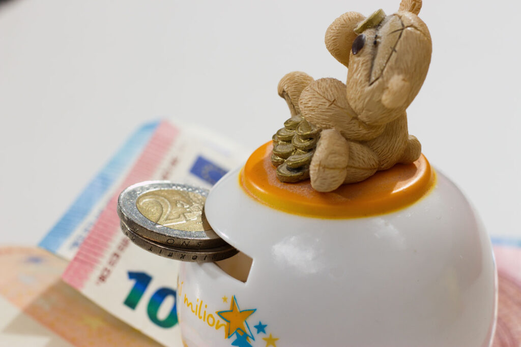 Zwei 2-Euro-Münzen und Papiergeld bei einer Spardose mit einem Bären.