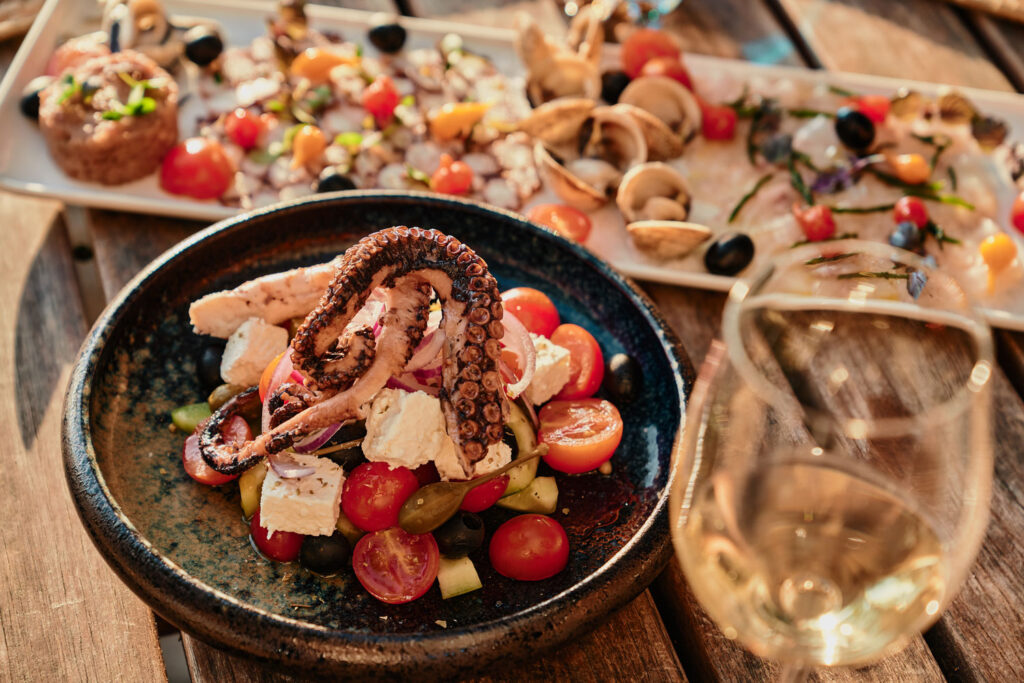Oktopus auf einem griechischen Salat mit Seafood-Platte im Hintergrund.