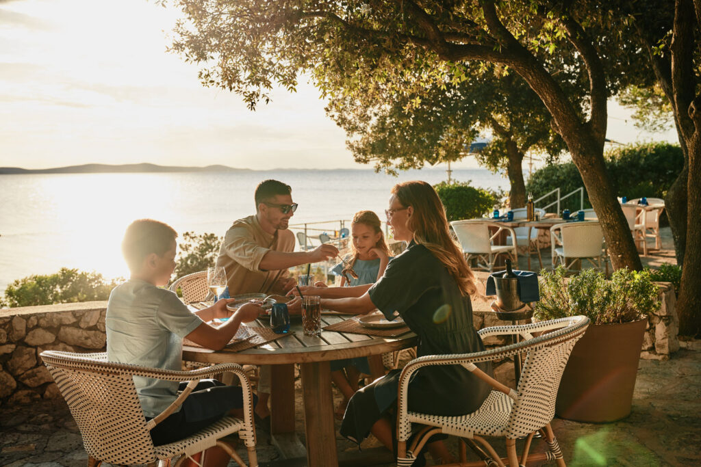 Familie isst im Gartenbereich mit Meerblick im Falkensteiner Hotel & Spa Iadera.