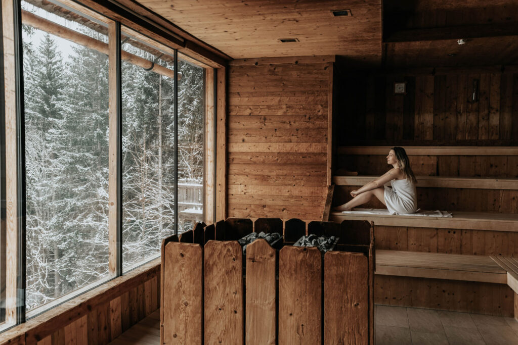 Frau sitzt in Sauna mit Blick auf verschneiten Wald im Hotel Höflehner.