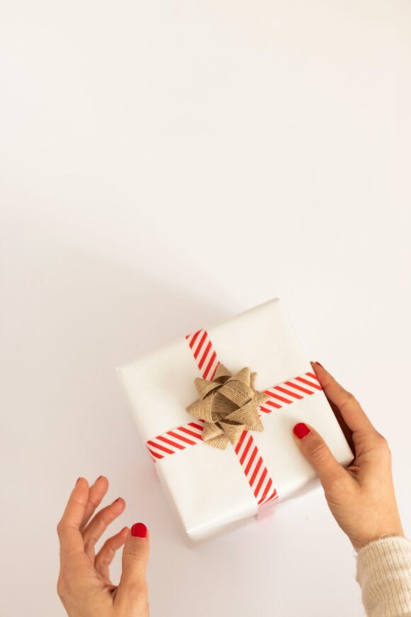 Last Minute Geschenke: HÃ¤nde halten ein weiÃes PÃ¤ckchen mit rotem Band und goldener Schleife
