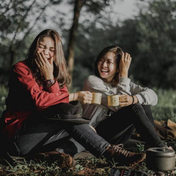 Zwei Frauen sitzen in der Natur und lachen