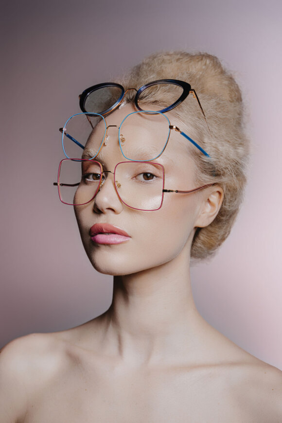 Brillenshooting: Blondes Model mit hochgesteckten Haaren und drei Billen am Kopf vor rosa Hintergrund