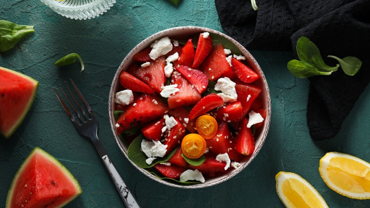 Erfrischende Sommerrezepte: SchÃ¼ssel mit Wassermelone und Feta. Steht auf grÃ¼nem Hintergrund. Es liegen WassermelonenstÃ¼cke und ZitronenstÃ¼cke daneben.