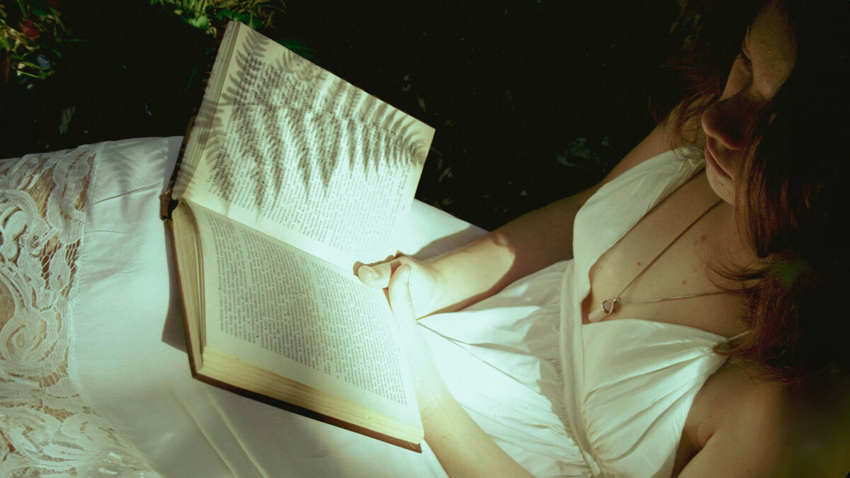 BÃ¼cher: Bild von oben von einer jungen Frau im weiÃen Sommerkleid, die ein geÃ¶ffnetes Buch in den HÃ¤nden hÃ¤lt.